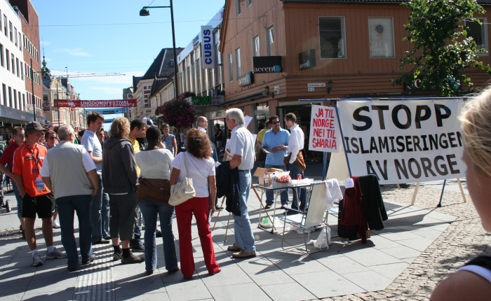 Her fra en tidligere SIAN-markering i Kristiansand. Det er stor interesse for det Stopp islamiseringen av Norge står for. Ingen andre organisasjoner, partier eller grupperinger tør å si sannheten om islam. Ola og Kari blir målløse når de får dokumentasjonen. De norske muslimene blir rasende - de hadde brukt vold hvis de hadde bodd i et muslimsk land - det gjør de ikke - ikke ennå.